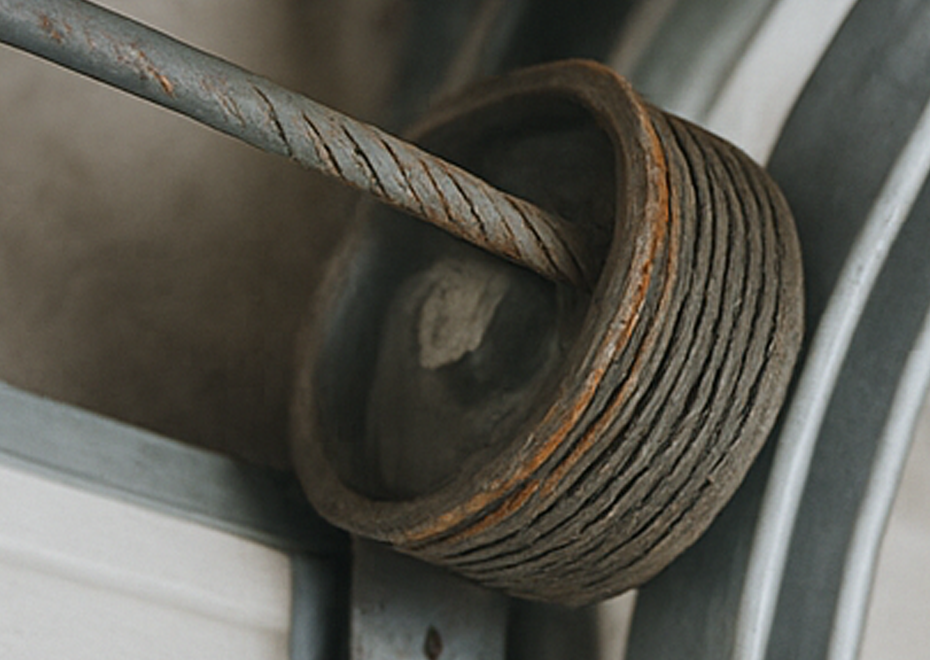 Close-up of frayed and rusted garage door cable wrapped around a drum